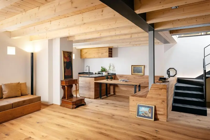 La zona giorno al piano terra: cucina, tavolo da otto e divano sotto le travi a vista